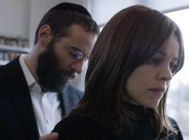 cena do filme desobediencia, em que um homem judeu está de cabeça baixa e uma mulher a sua frente de costas, com olhar triste