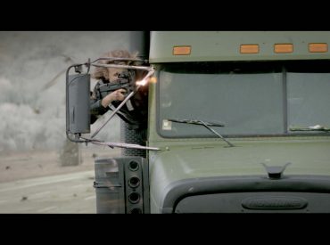 Homem atirando, com a cabeça pra fora da janela de um caminhão, cena do filme "no olho do furacão"