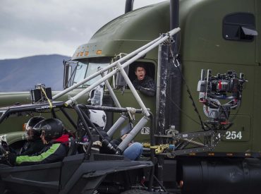 Cena dos bastidores do filme "no olho do furacão", gravação de um caminhão em movimento e o câmera acompanhando em um veículo adaptado parecido com um triciclo.