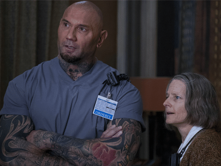 foto de divulgação do filme hotel artemis. home alto e forte com roupa de médico ou enfermeiro e uma mulher de cabelos grisalhos ao lado com um estetoscópio pendurado no pescoço