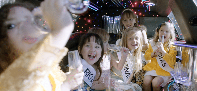 cena do filme "mini miss" com várias criançar bebendo champanhe em uma limousine