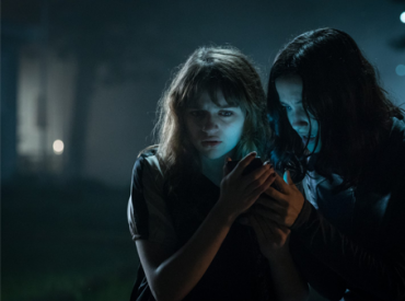 Cena do filme "Slender Man" em que duas meninas estão olha um celular em um local escuro na rua