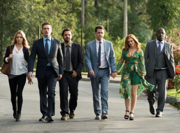 Cena do filme "Te Peguei". Com seis pessoas vestidas para festa, caminhando paralelamente em uma rua arborizada.