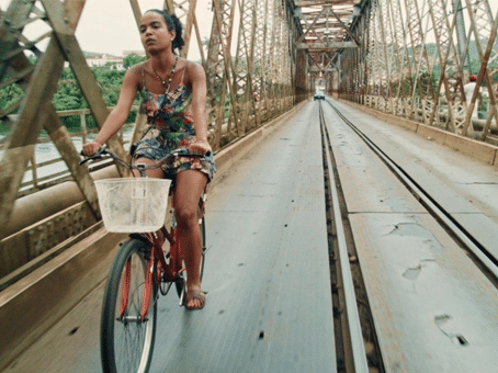 foto divulgação do filme "Café com Canela". Mulher negra andando de bicicleta em uma ponte