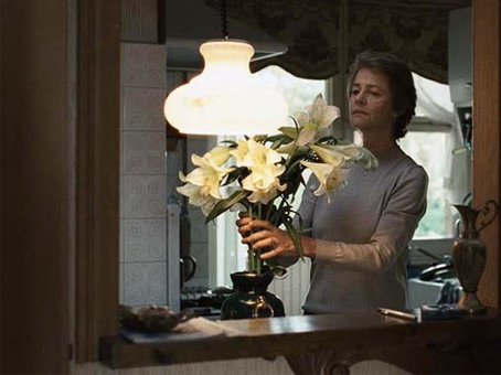 foto divulgação do filme Hannah. mulher ajeitando flores em um vaso. foto tiranda do espelho em que reflete a mulher