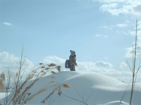 foto divulgação do filme "Takara a noite em que nadei". Menininho oriental com roupas para frio intenso, no meio da neve, olhando para o horizonte.
